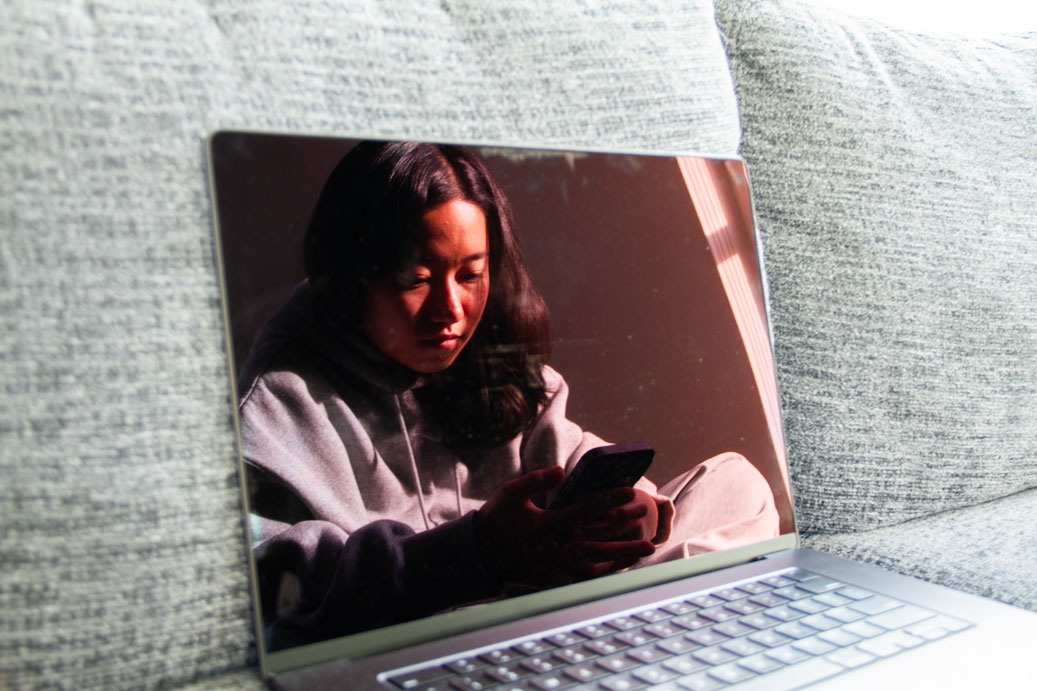 Photo of girl on her phone reflected in a laptop screen on a sunny day